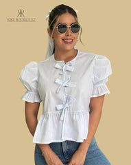 Mujer vistiendo la Blusa Sofía Blanca de Kike Rodriguez con diseño peplum, lazos frontales y mangas tres cuartos, ideal para un look casual y elegante
