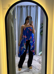 Mujer vistiendo una blusa larga de tirantes con estampado floral azul, posando frente a un espejo con un entorno moderno y elegante de fondo.