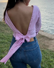 Mujer con blusa rosa con espalda descubierta disfrutando de una vista panorámica. Blusa ideal para un look casual y sofisticado. Disponible en KIKE RODRIGUEZ.