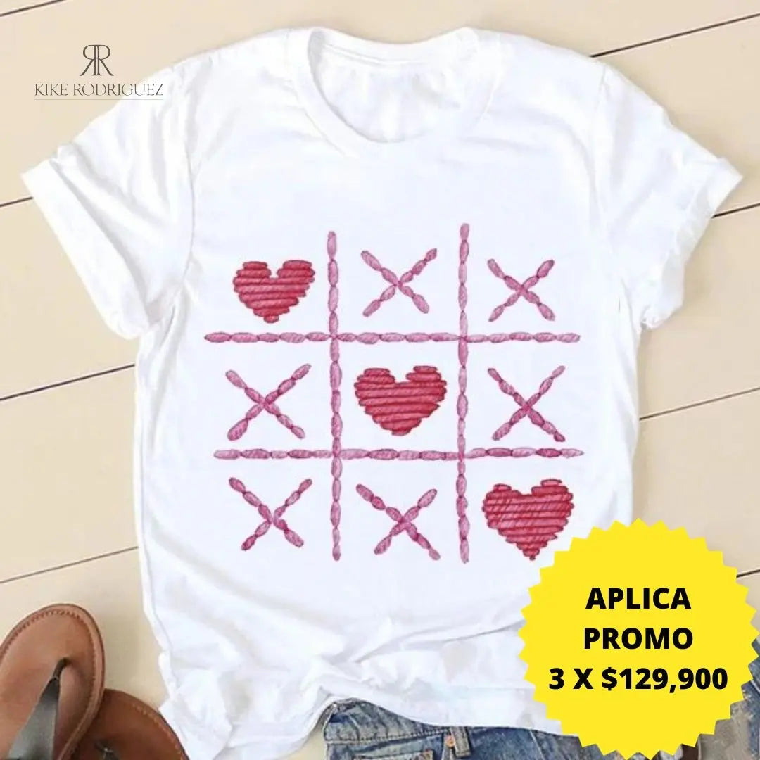 Camiseta blanca con un creativo estampado de tres en raya con corazones rojos. Disponible en promoción de 3 por $129,900 en KIKE RODRIGUEZ. Perfecta para un look casual y romántico. ¡Ideal para cualquier ocasión!