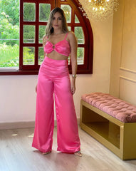 Mujer vistiendo un conjunto Rosa Barbie de KIKE RODRIGUEZ, compuesto por un top con aro y pantalones anchos, posando en un entorno elegante con una ventana y una lámpara de fondo.
