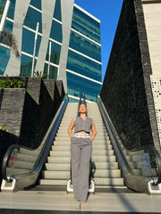 Mujer vistiendo un conjunto de pantalón y chaleco gris de KIKE RODRIGUEZ, posando en una escalera moderna con un fondo arquitectónico y vegetación.