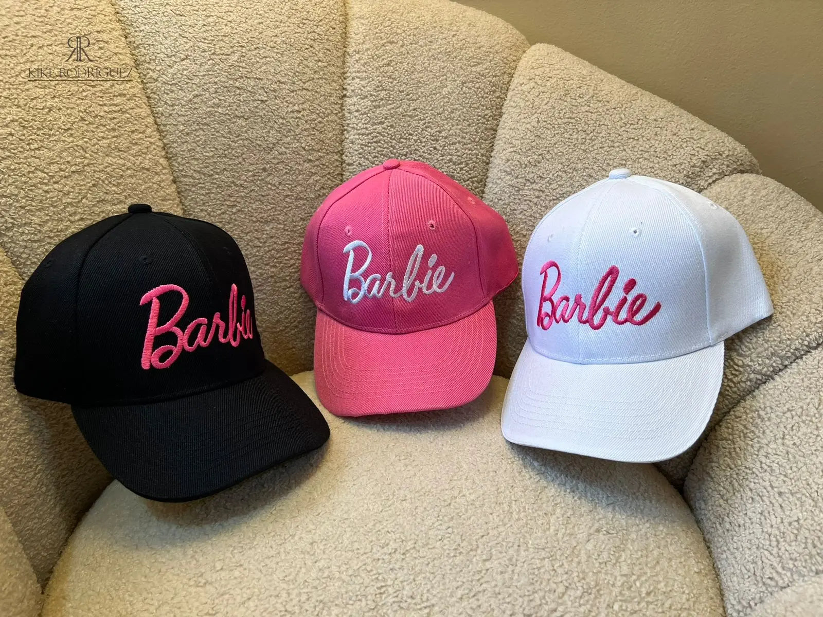 Gorra fucsia de Kike Rodriguez con el logo de Barbie en blanco, acompañada de gafas de sol rosas sobre un fondo de peluche, ideal para un look femenino, moderno y divertido