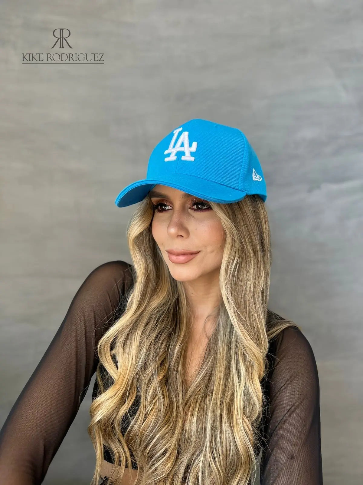 Mujer usando una gorra azul cielo de Kike Rodriguez con logo blanco de Los Angeles Dodgers, combinada con top de malla negra, ideal para un look moderno y casual