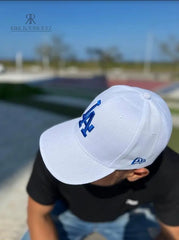 Hombre usando una gorra blanca de Kike Rodriguez con logo azul de Los Angeles Dodgers, combinada con gafas de sol y camiseta negra, ideal para un look deportivo y elegante