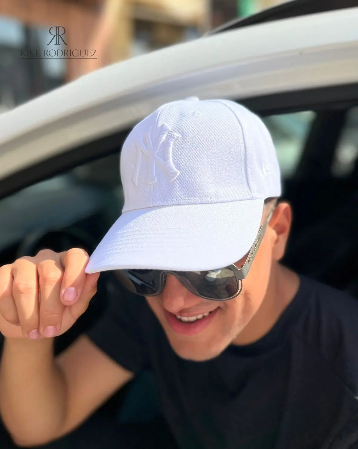 Hombre usando una gorra blanca de Kike Rodriguez con logo blanco de los New York Yankees, combinada con gafas de sol y camiseta negra para un look casual y moderno