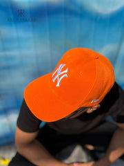 Hombre usando una gorra naranja de Kike Rodriguez con logo blanco de los New York Yankees, combinada con gafas de sol y camiseta negra para un look deportivo y moderno