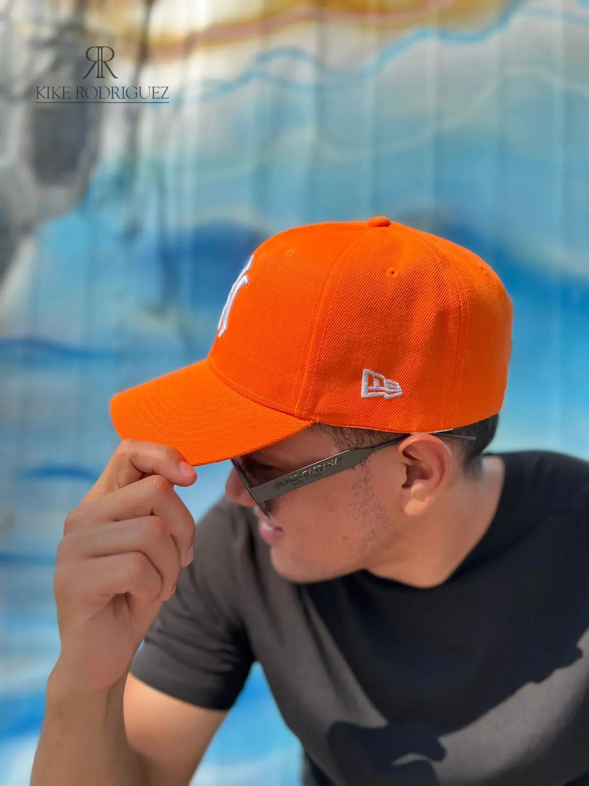 Hombre usando una gorra naranja de Kike Rodriguez con logo blanco de los New York Yankees, combinada con gafas de sol y camiseta negra para un look deportivo y moderno