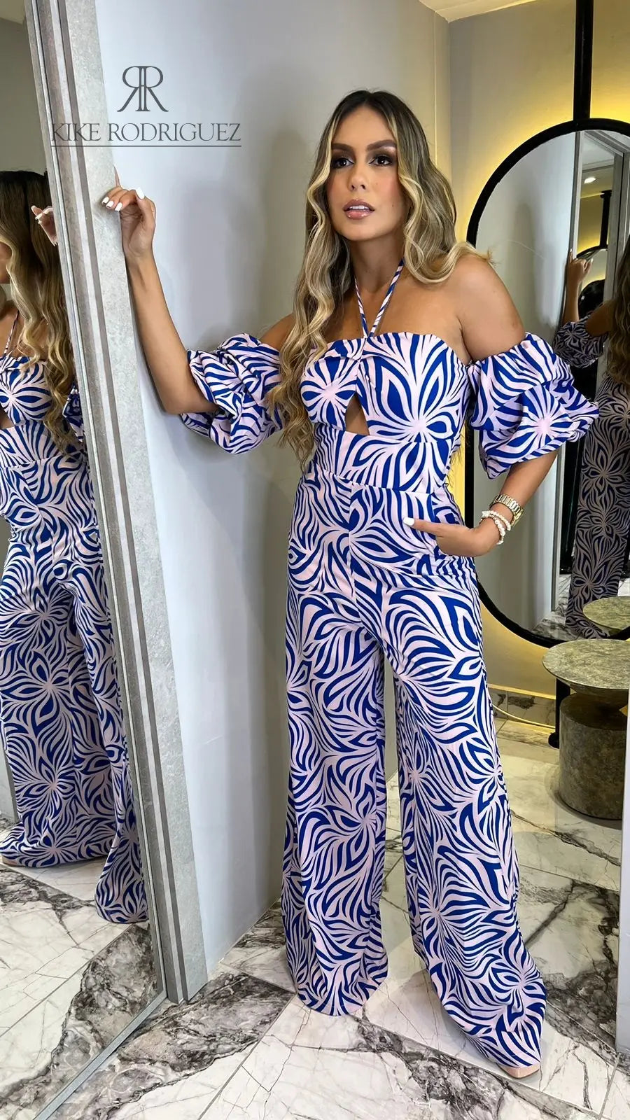 Modelo luciendo un moderno enterizo con estampado azul y rosa, escote halter y mangas abullonadas, ideal para destacar en cualquier evento.