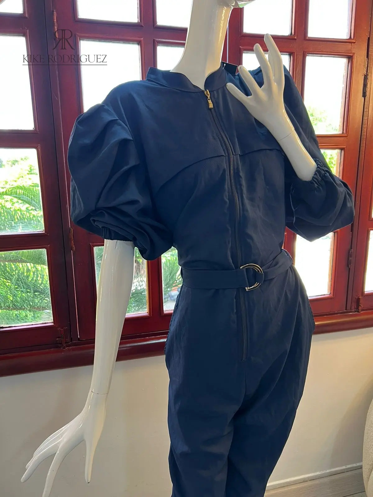 Maniquí luciendo un elegante mono azul con mangas abullonadas y cinturón ajustable, ideal para ocasiones especiales o salidas casuales con estilo.