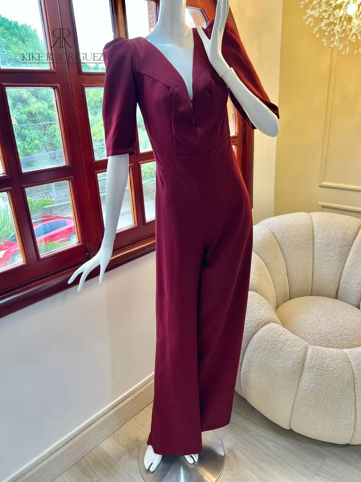 Maniquí luciendo un elegante mono vinotinto con mangas abullonadas, una prenda perfecta para eventos especiales y ocasiones formales de KIKE RODRIGUEZ.