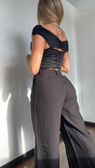 Mujer luciendo un top negro asimétrico con detalle de flor, perfecto para un look sofisticado y moderno. Disponible en KIKE RODRIGUEZ.