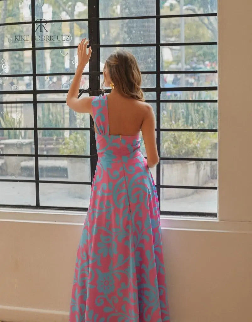 Mujer luciendo un vestido largo floral en rosa y azul de KIKE RODRIGUEZ, destacando elegancia y estilo para eventos especiales.
