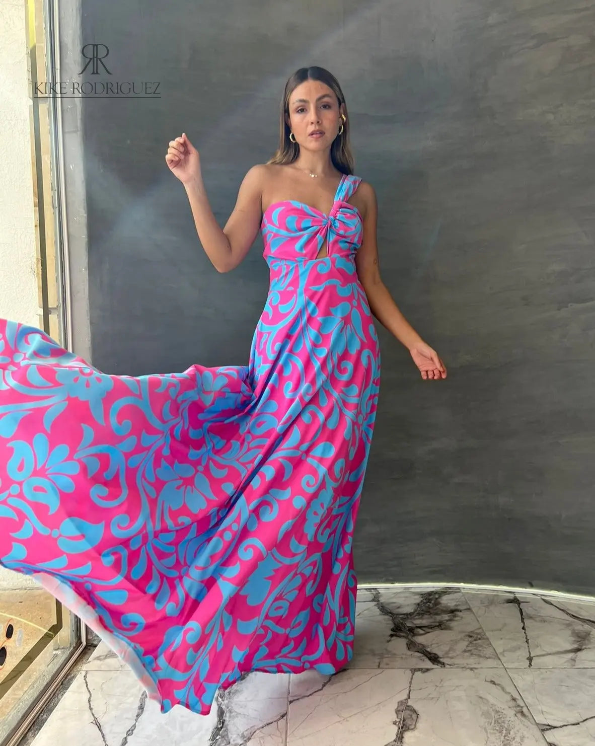 Mujer luciendo un vestido largo floral en rosa y azul de KIKE RODRIGUEZ, destacando elegancia y estilo para eventos especiales.