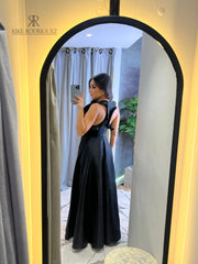 Mujer posando frente al espejo con un vestido largo negro, con escote en V y detalles recortados, ideal para eventos formales y ocasiones especiales.