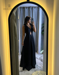 Mujer posando frente al espejo con un vestido largo negro, con escote en V y detalles recortados, ideal para eventos formales y ocasiones especiales.