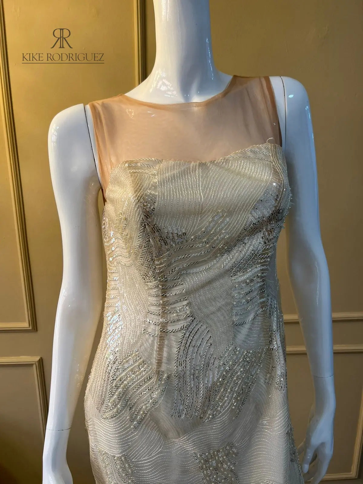 Maniquí vistiendo un elegante vestido de fiesta en color beige con detalles de lentejuelas, ideal para eventos especiales y celebraciones.