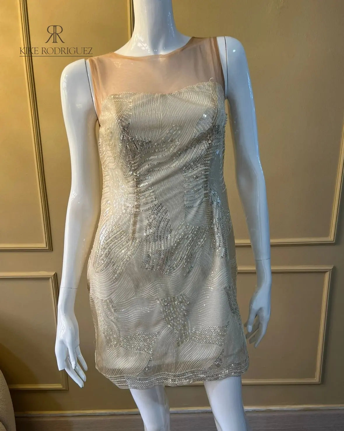 Maniquí vistiendo un elegante vestido de fiesta en color beige con detalles de lentejuelas, ideal para eventos especiales y celebraciones.