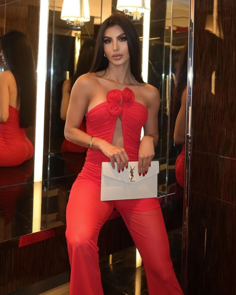 Mujer usando enterizo rojo con escote profundo y flores 3D, pantalón elegante y clutch blanco – KIKE RODRIGUEZ.