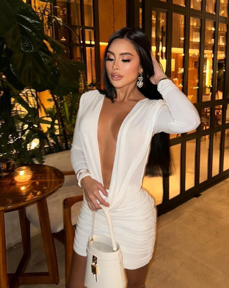 Mujer de pie con el Vestido Furia blanco, mostrando detalles drapeados y bolso estructurado.